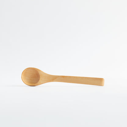 A light natural wood spoon with a smooth, rounded bowl and a simple rectangular handle, resting horizontally on a seamless white background.